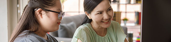 A woman and a student with down syndrome looking into a computer screen.